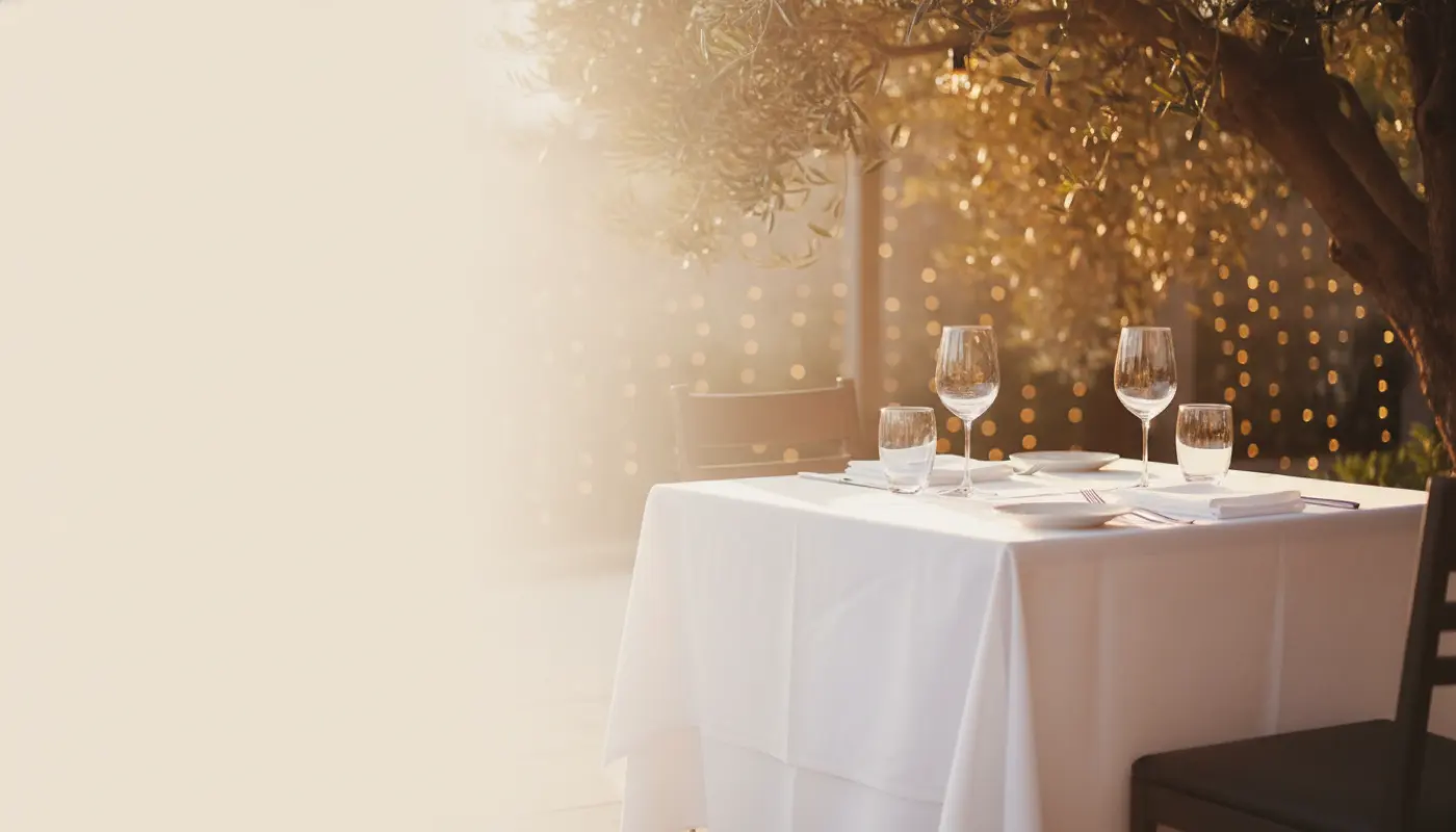 A set restaurant patio table at golden hour under an olive tree